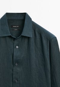 Dark teal linen shirt featuring a spread collar, long sleeves, and five buttons down the front. Label displays brand and fabric information.