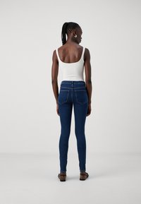 Λεπτά μπλε τζιν με ψηλή μέση και πλαϊνές τσέπες, συνδυασμένα με ένα λευκό ριμπ μπλουζάκι, με θέα από πίσω.