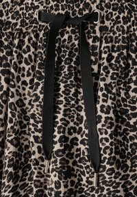 Leopardskinnemönstrad tyg med en beige botten och svarta fläckar; har en svart snörning med metallspetsar vid midjan.