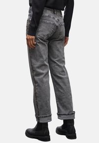 Jeans en denim gris avec une coupe décontractée, ourlets retroussés et un accent doré le long des coutures latérales. Les poches arrière présentent un design classique.