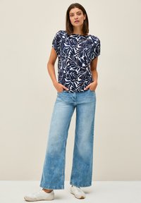 Marinblus med vit bladmotiv och korta ärmar, tillsammans med ljusblå vida jeans och vita sneakers. Subtil textur i tyget.