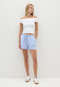 Top corto blanco sin hombros combinado con pantalones cortos a rayas azul claro. Los pantalones cortos tienen una cinturilla elástica y un ajuste relajado. Unos zapatos deportivos completan el look.