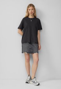 Zwarte oversized t-shirt met opgerolde mouwen, gecombineerd met een grijze denim minirok met een rafelige zoom, gedragen met metallic sneakers.