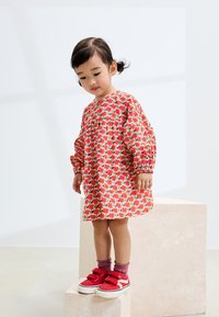 Farverig børnekjole med lange pufærmer, der har et blomstermønster i rød, pink og grøn. Røde sneakers og ribstrikkede pink sokker fuldender outfittet.