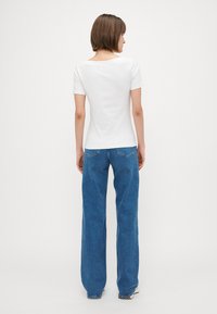 Hvit kortermet topp kombinert med høyt liv og vide blå jeans, med lapplommer og rett silhuett.