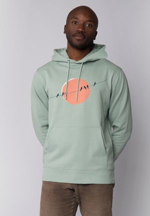 Mintgroene hoodie met een cirkelvormige perzikafbeelding en zwarte vogels op een draad ontwerp, met een zak aan de voorkant en een trekkoordkap.