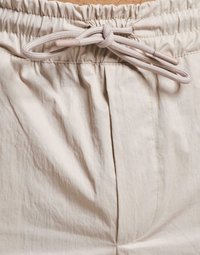 Shorts beige clair à taille élastique avec cordon de serrage, présentant un tissu texturé et des poches latérales. Les coutures sont visibles sur les seams.