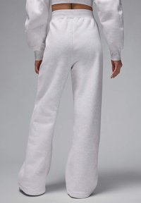 Pantalones de chándal sobrecogidos de color gris claro, hechos de una tela suave. Diseño de talle alto y acampanado con cinturilla elástica y detalles de costura visibles.