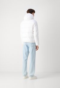 Vit puffjacka med hög krage och huva, med sydda sektioner; matchad med ljusblå jeans och vita skor.