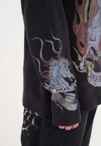 Zwarte lange mouwen shirt met grafische ontwerpen van een paard en vlammen op de mouw, met het woord "DEAD" op een lint. Gelaagde stof.
