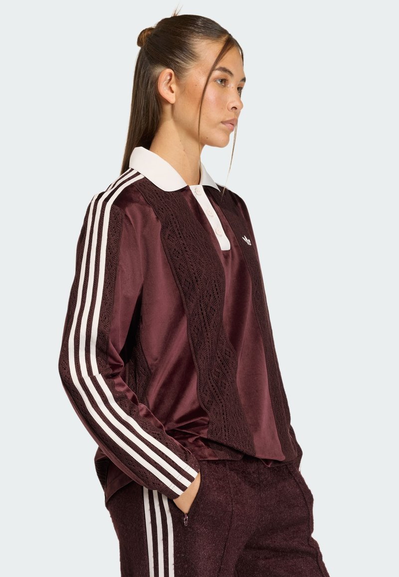 Bordeaux rood poloshirt met lange mouwen, een witte kraag en knoopsluitingen. Beschikt over textuurpatronen en drie witte strepen op elke mouw.