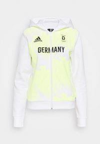 Sweat à capuche jaune-vert avec manches blanches, équipé d'une fermeture éclair devant, "GERMANY" en texte noir gras, et logo Adidas sur le côté supérieur gauche.