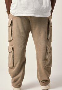 Beige cargobroek gemaakt van ribbelstof, met meerdere zijzakken, een losse pasvorm en opgerolde enkels. Gekenmerkt door subtiele naden.