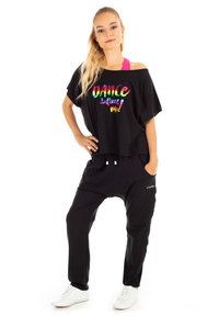 Crni oversized majica s dugim rukavima s dušom "DANCE defining me!" u duginim bojama, uparen s crnim trenerkama; oboje je izrađeno od mekog, rastezljivog materijala.