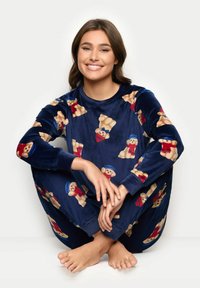 Pigiama in morbido velluto blu navy con motivo di orsetti teddy in rosso e blu. Maniche lunghe e design ampio con polsini a coste.
