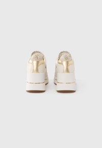 Par de ténis plataforma brancos e dourados vistos por trás, com tecido estampado e detalhes de logotipo na gola do calcanhar.