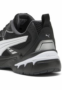 Black athletic shoe with mesh upper, white accents, padded collar, and textured sole. Features a prominent logo on the heel.