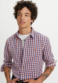 Camisa de cuadros de manga corta en tonos rojo, azul y blanco, con collar abotonado y logo de Levi's en el bolsillo del pecho. Fabricada en tejido ligero.