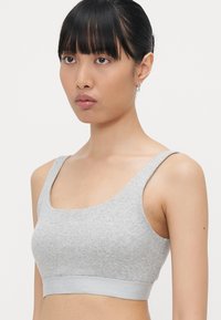 Šedý žebrovaný bralet s širokými ramínky a širokým páskem se znakem "Organic Basics". Materiál má jemnou texturu a close-fitting design.