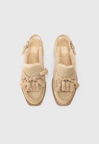 Sapatos de camurça bege com biqueira fechada, design slingback, acentuados por franjas e borlas, apresentando um interior suave forrado a lã.