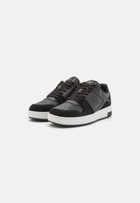 Zapatillas negras que combinan cuero liso y ante, con detalles de perforación en la punta, cordones en tono y una suela de goma blanca.