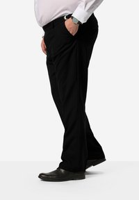 Černé kalhoty s přiléhavým střihem, s předními kapsami a hladkou texturou, spárované s černými botami a stříbrnými hodinkami.