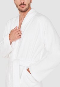 Bata de baño de rizo blanca con mangas largas y cinturón en la cintura, que cuenta con bolsillos laterales y una superficie texturizada.