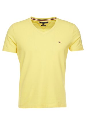 Żółta koszulka z krótkim rękawem i dekoltem w serek, z małym logo Tommy Hilfiger na lewej piersi oraz paskowanym detalem wewnątrz kołnierza.