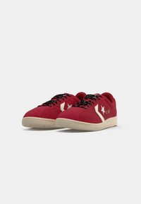 Red suede sneakers with black laces, a white star logo, and cream-colored sole. Low-top design, smooth texture, and clean lines.