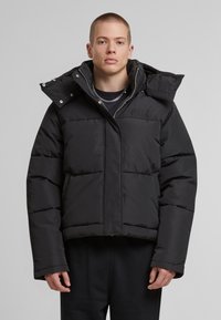 Černá péřová bunda s krátkým střihem, prošívanou texturou a vysokým límcem. Obsahuje přední zip a vyšívané logo na hrudi.