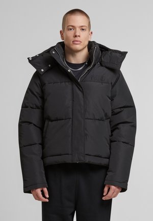 Svart pufferjakke med cropped-design, quiltet tekstur og høy krage. Har en frontglidelås og brodert logo på brystet.