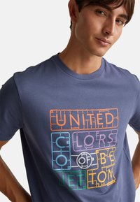 Camiseta de manga corta, de color azul marino, hecha de algodón, con un texto gráfico multicolor "UNITED COLORS OF BENETTON" en fuentes gruesas y juguetonas.