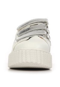 Sneakers bianchi con suola in gomma texturizzata. Presentano tre cinturini in velcro argentati sulla parte superiore. Materiale liscio con punta arrotondata.