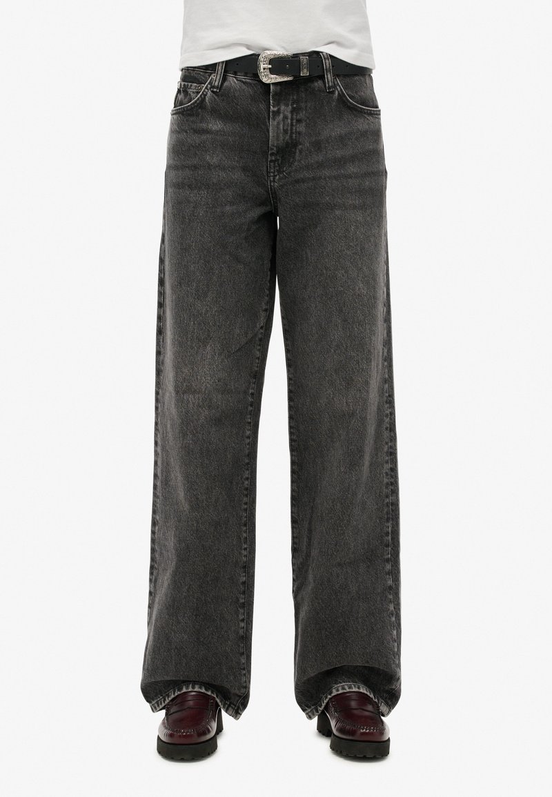 Jean noir à jambes larges avec une taille haute, dotée d'une fermeture classique à bouton et à zip, et d'une texture légèrement délavée.