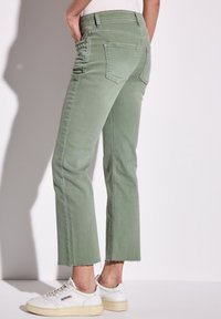Minzgrüne, hoch taillierte, kurz geschnittene Jeans mit rohem Saum, mit Gesäßtaschen ausgestattet und kombiniert mit weißen Sneakers. Glatte Textur.