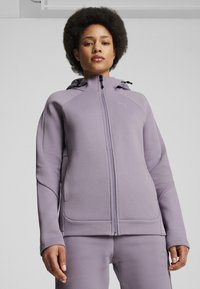 Sudadera con cremallera púrpura, con capucha, que presenta mangas texturizadas, bolsillos laterales y un pequeño logo en el pecho. Tela suave con un corte holgado.