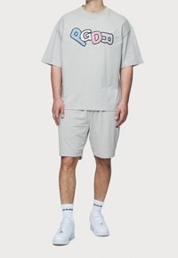 Camiseta gris de gran tamaño con un diseño gráfico multicolor, combinada con pantalones cortos grises texturizados y zapatillas blancas, que llevan calcetines hasta el tobillo.