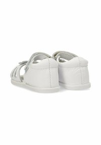 Sandalias de cuero blanco con diseño recortado, acentos grises y suela plana. Las correas se ajustan para un uso seguro. La vista trasera destaca la costura.