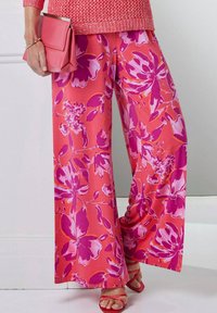 Pantalon large à fleurs roses avec de grandes fleurs violettes et blanches, conçu en tissu léger, associé à une pochette rose assortie.