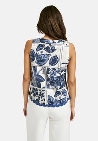 Ärmelloses Oberteil mit Blumenmuster in Weiß und Marineblau, mit gewelltem Saum und einer Schlüsselloch-Knopfleiste im Rücken. Leichter Stoff.