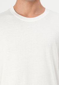 T-shirt branca de algodão com decote redondo e mangas curtas. O tecido tem uma aparência ligeiramente texturizada e suave. Sem padrões ou gráficos visíveis.