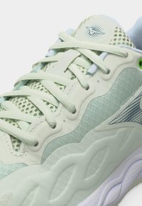 Αθλητικό παπούτσι ανοιχτού πράσινου χρώματος με πλέγμα ύφασμα, υφή σόλας και κορδόνια δεμένα πάνω από μια επενδεδυμένη γλώσσα με μικρό λογότυπο.