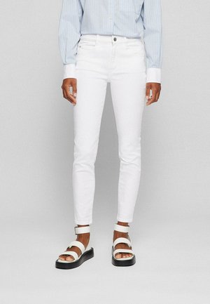 Jean skinny en denim blanc avec cinq poches, une fermeture à bouton, associés à des sandales blanches à larges brides et à une semelle noire épaisse.