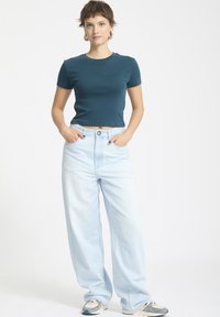 Türkisfarbenes, tailliertes T-Shirt mit kurzen Ärmeln und Rundhalsausschnitt, kombiniert mit hellblauen Schlagjeans und mehrfarbigen Sneakers.