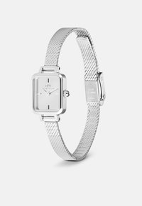 Montre carrée en argent avec un cadran blanc, présentant des index d'heure noirs, un bracelet en métal maillé et une boucle en acier inoxydable. Design minimaliste.