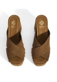 Sandales ouvertes en suède marron avec un design entrelacé, un léger talon et un détail de marque doré. Doublure intérieure lisse et accents de couture.