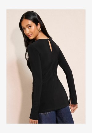 Czarna bluzka z długim rękawem i dekoltem w kształcie łezki, charakteryzująca się dopasowanym krojem i miękką teksturą. Noszona z niebieskimi dżinsami.