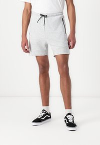 Grå bomullsblandingsshorts med elastisk midje og snor, med sidelommer med glidelås og en avslappet passform. Brukt med svarte joggesko.