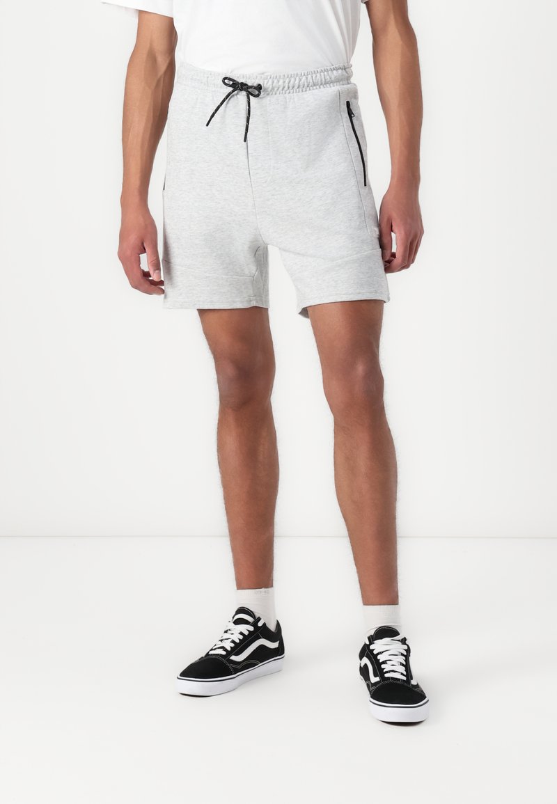 Grå bomullsblandingsshorts med elastisk midje og snor, med sidelommer med glidelås og en avslappet passform. Brukt med svarte joggesko.