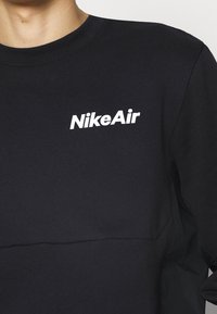 Svart sweatshirt gjord av bomullsblandat tyg, med rund halsringning och "NikeAir"-logotyp i vitt på den övre vänstra sidan.